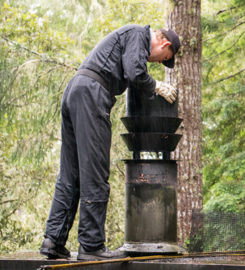 Chimney sweep in protective gear performing outdoor chimney cleaning and maintenance